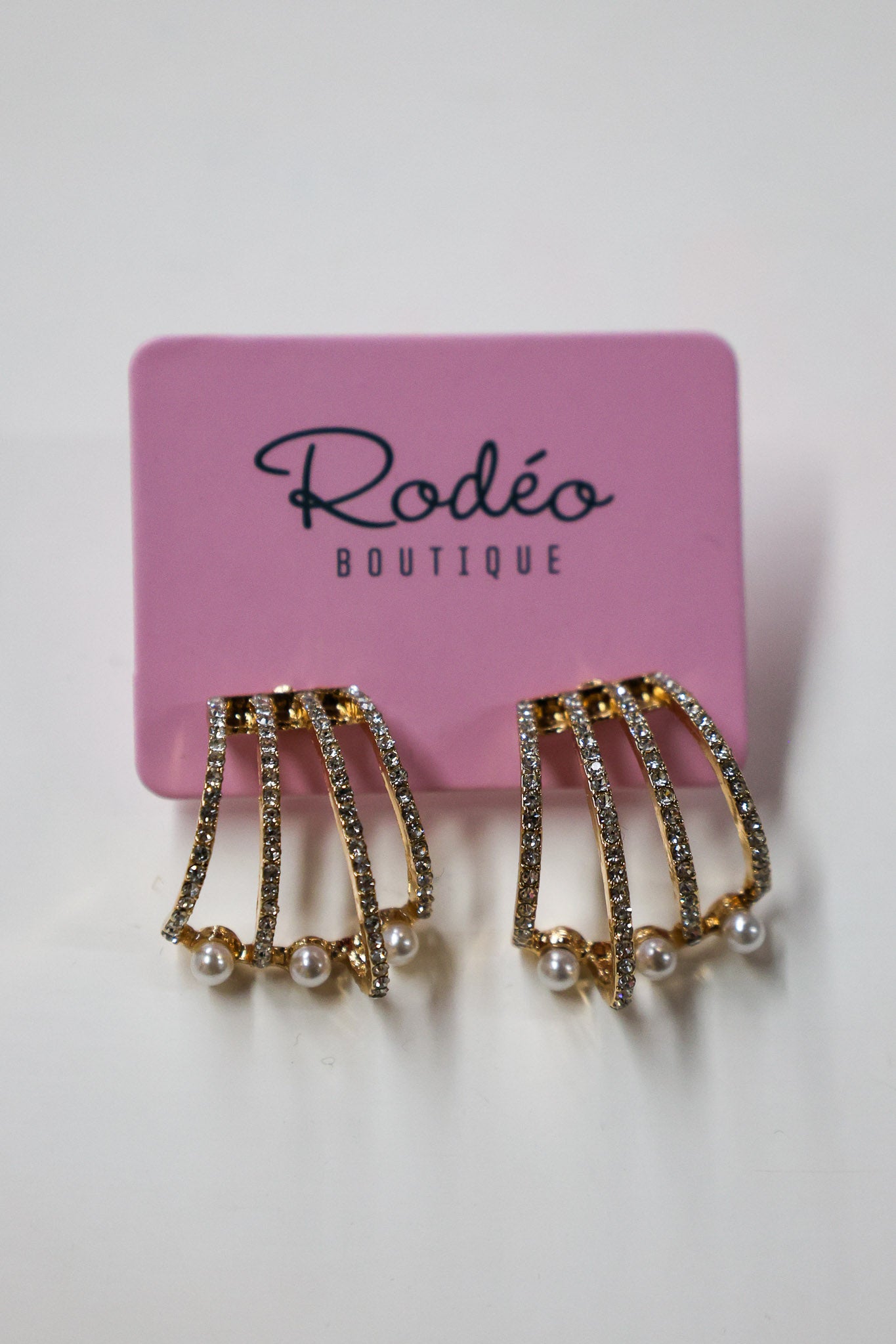 Pair of gold and pearl earrings on a pink card with 'Rodeo Boutique' branding.