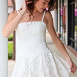 Woman wearing a white eyelet lace dress standing outdoors.