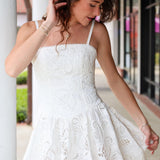 Woman wearing a white eyelet lace dress standing outdoors.
