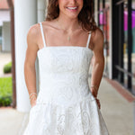 Woman wearing a white eyelet lace dress standing outdoors.