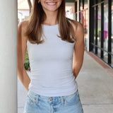 Woman wearing a light blue tank top and denim shorts standing outdoors.