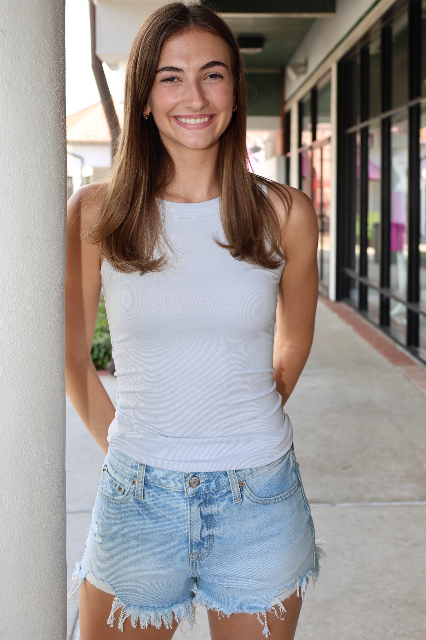 Woman wearing a light blue tank top and denim shorts standing outdoors.