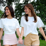 Two women walking hand-in-hand on a path with trees and a lake in the background.