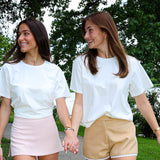 Two women walking hand-in-hand on a path with trees and a lake in the background.