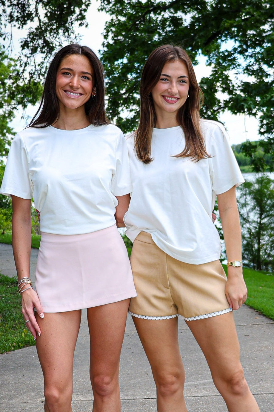 Two women standing on a path with trees and water in the background