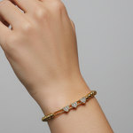 Gold bracelet with diamonds on a wrist against a gray background