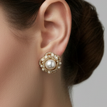 Close-up of an ear wearing a decorative earring with a pearl center on a neutral background