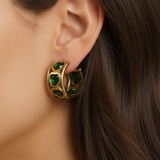 Gold earring with green heart gemstones worn by a person