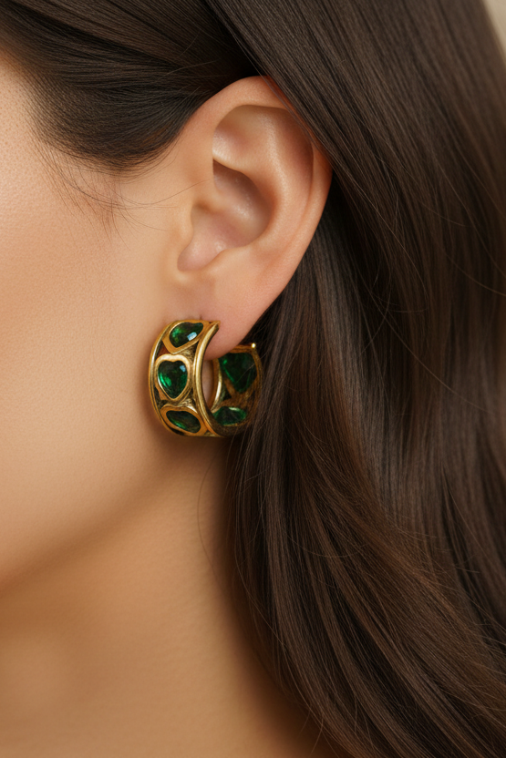 Gold earring with green heart gemstones worn by a person