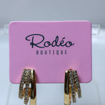 Gold huggie hoop earrings with clear rhinestone accents, displayed on a pink Rodéo Boutique card.