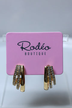 Gold huggie hoop earrings with clear rhinestone accents, displayed on a pink Rodéo Boutique card.