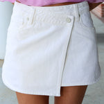 White denim wrap skirt worn with a pink top on a neutral background