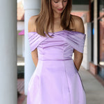 Woman wearing a light purple off-shoulder dress standing outdoors.