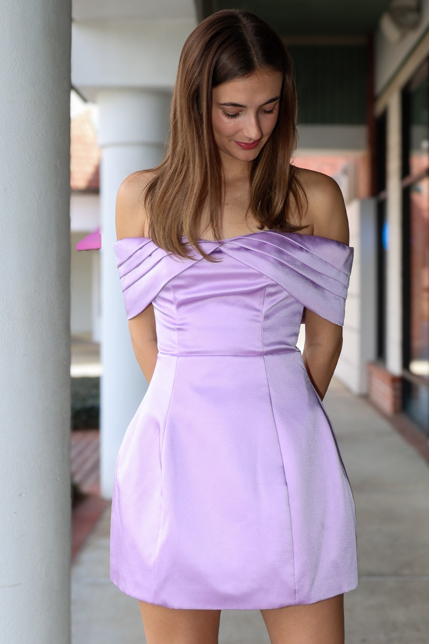Woman wearing a light purple off-shoulder dress standing outdoors.