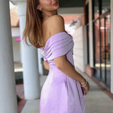 Woman in a light purple off-shoulder dress standing outdoors.