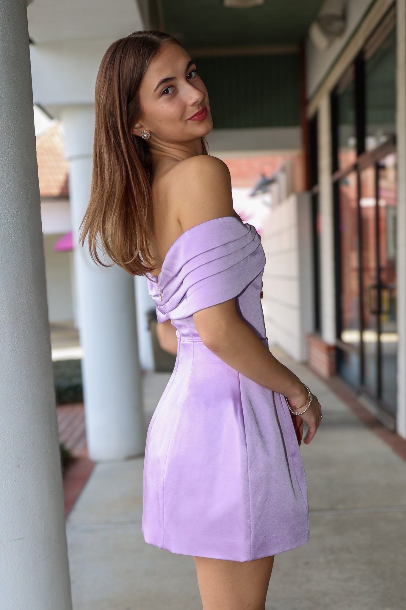 Woman in a light purple off-shoulder dress standing outdoors.