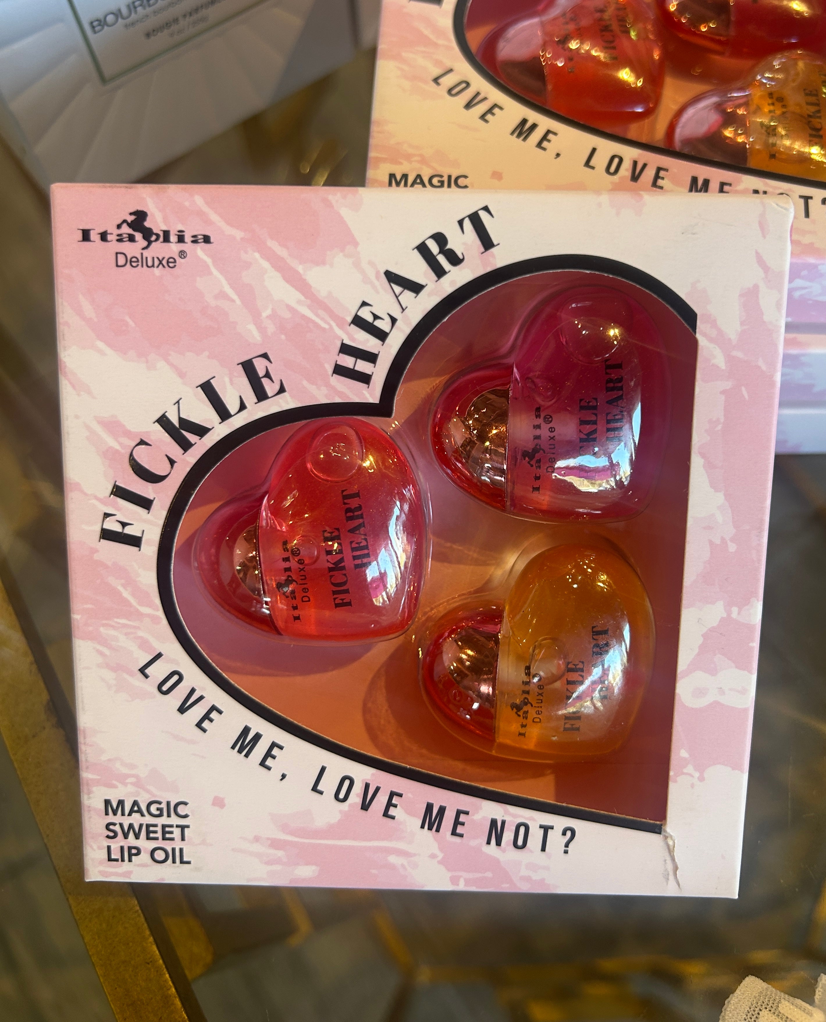 Heart-shaped lip oils in a box with 'Fickle Heart' branding on a reflective surface.