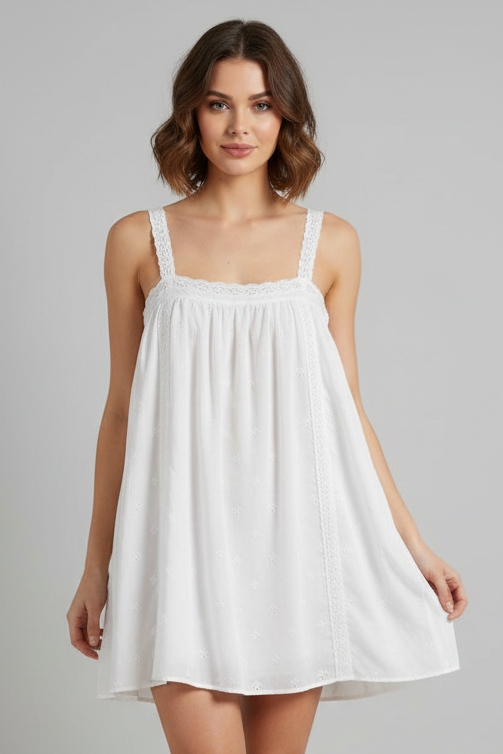 Woman wearing a white eyelet babydoll style mini dress against a plain background