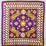 A square purple silk scarf with a gold and white checkered border, featuring four yellow leopards and white flowers in the center