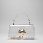 A clear vinyl handbag with a curved top handle, gold-tone hardware, and a prominent metallic gold geometric clasp, photographed on a neutral light gray background.