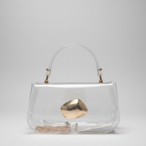 A clear vinyl handbag with a curved top handle, gold-tone hardware, and a prominent metallic gold geometric clasp, photographed on a neutral light gray background.