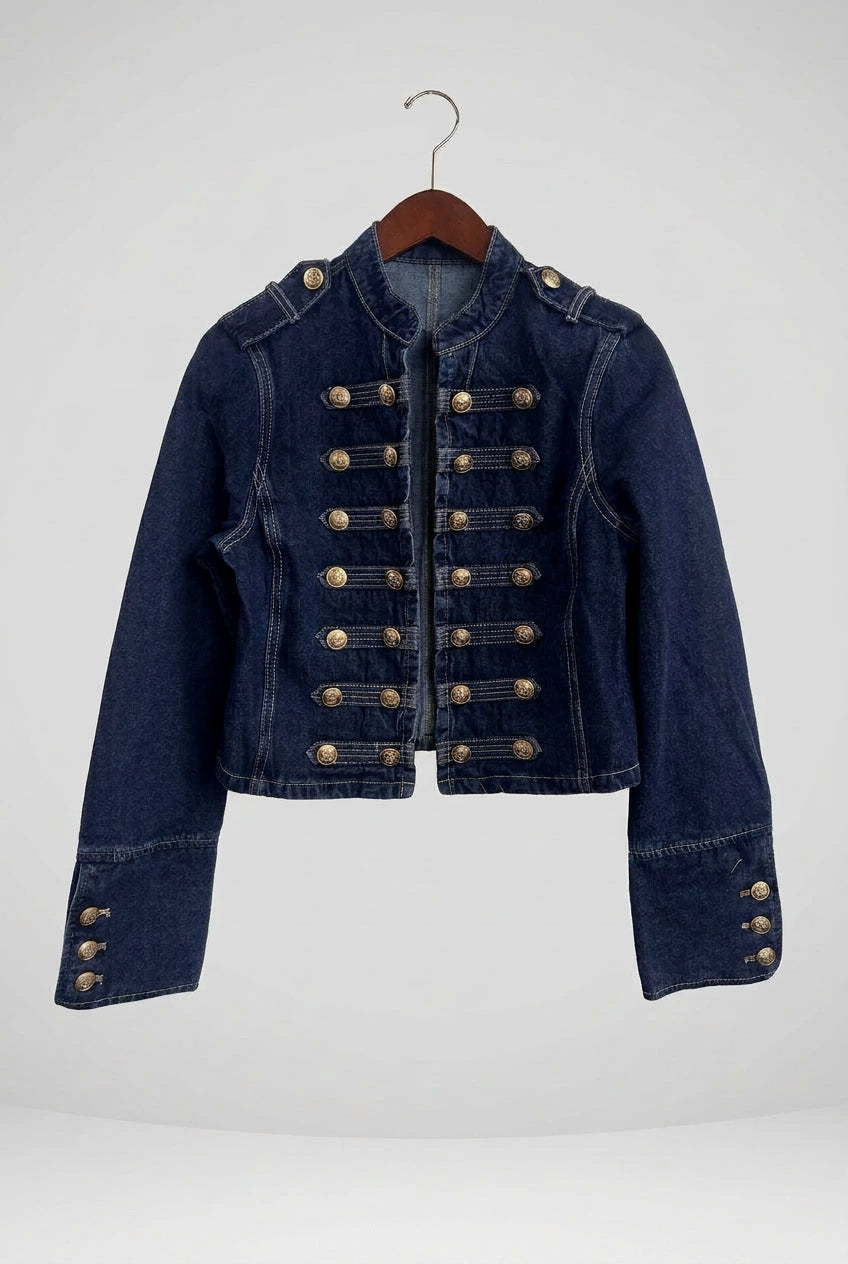 A dark blue denim jacket with decorative gold-colored military-style buttons, shown hanging on a wooden hanger against a white wall.