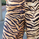 Close-up of a person wearing tiger-print pants with a beige base and bold black stripes, shown from the waist down.