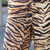 Close-up of a person wearing tiger-print pants with a beige base and bold black stripes, shown from the waist down.