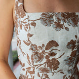 Close-up of a woman wearing a sleeveless top with a square neckline and a brown floral jacquard pattern on a light beige fabric.