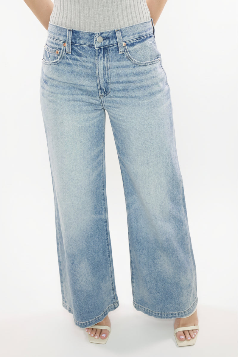 A pair of Jadyn low slung palazzo jeans with a medium wash. The jeans are on a model who is standing, showing the wide-leg style and fit.