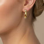 A pair of gold hoop earrings with small clear crystal accents, displayed on a pink card labeled 'Rodeo Boutique'.