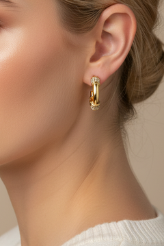 A pair of gold hoop earrings with small clear crystal accents, displayed on a pink card labeled 'Rodeo Boutique'.