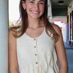 Woman wearing a cream-colored sleeveless top with buttons, standing outdoors.