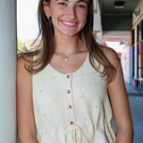 Woman wearing a cream-colored sleeveless top with buttons, standing outdoors.