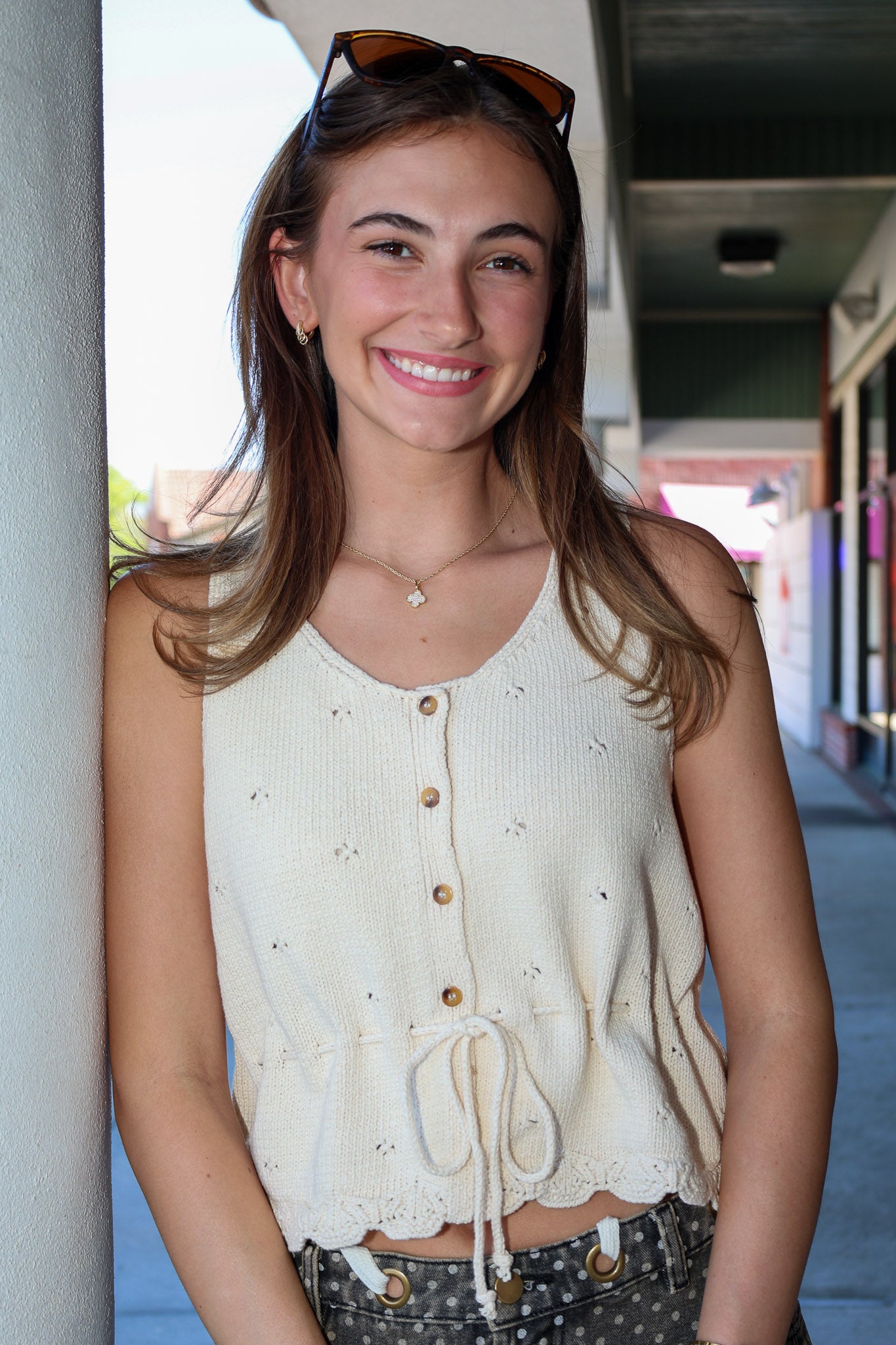 Woman wearing a cream-colored sleeveless top with buttons, standing outdoors.