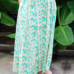 Person wearing a green and white patterned skirt standing against a leafy background