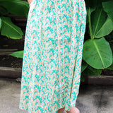 Person wearing a green and white patterned skirt standing against a leafy background