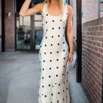 Woman wearing a white polka dot dress and black hat outdoors.