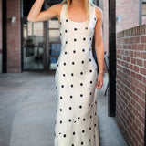 Woman wearing a white polka dot dress and black hat outdoors.