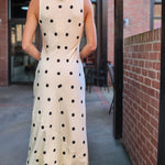 Woman wearing a polka dot dress and black hat walking away from the camera.