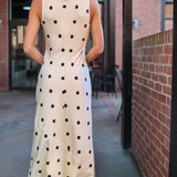 Woman wearing a polka dot dress and black hat walking away from the camera.