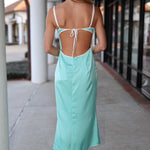 Woman wearing a light blue dress with thin straps and open back, walking on a sidewalk.