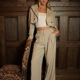 Woman in beige outfit standing in a room with wooden paneling and decorative elements.
