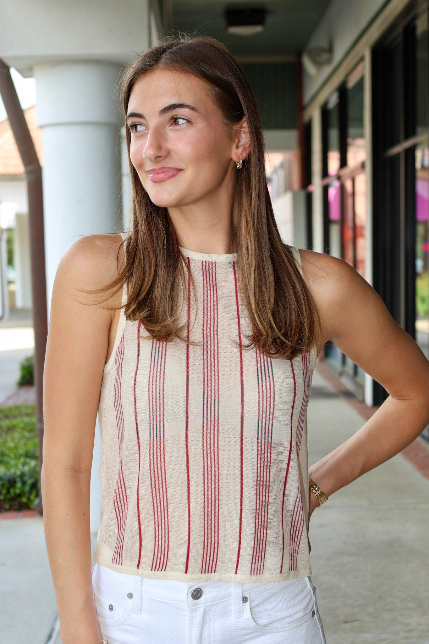 Woman wearing a striped sleeveless top and white pants outdoors.