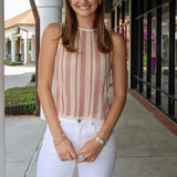 Woman wearing a striped sleeveless top and white pants standing on a sidewalk.