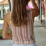 Woman wearing a striped tank top and white pants on a sidewalk.