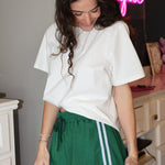 Woman wearing a white oversized t-shirt and green shorts with white lace trim in an indoor setting.