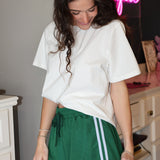 Woman wearing a white oversized t-shirt and green shorts with white lace trim in an indoor setting.