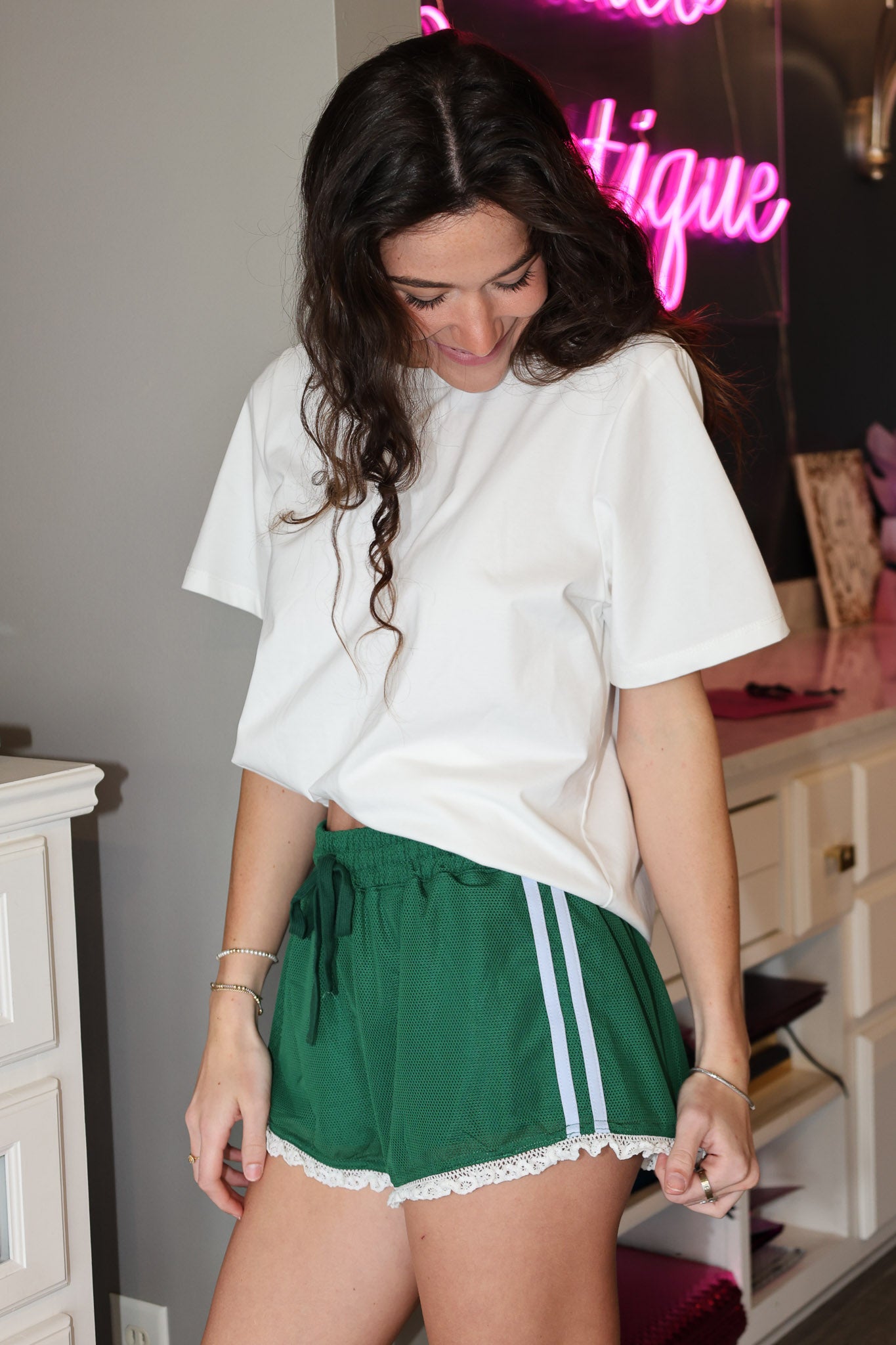 Woman wearing a white oversized t-shirt and green shorts with white lace trim in an indoor setting.