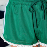 Green shorts with lace trim worn by a person indoors.
